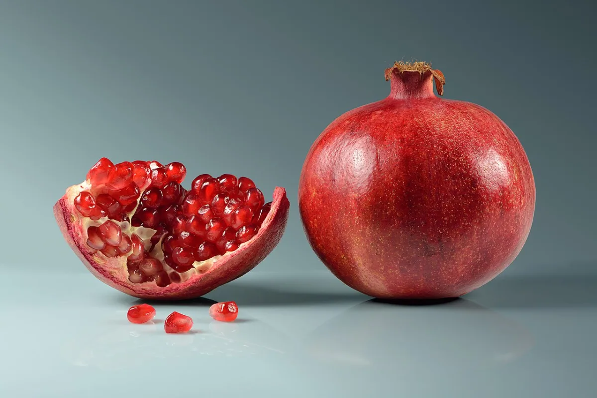 Een opengesneden granaatappel met glanzende rode pitjes zichtbaar tussen het witte vruchtvlies.