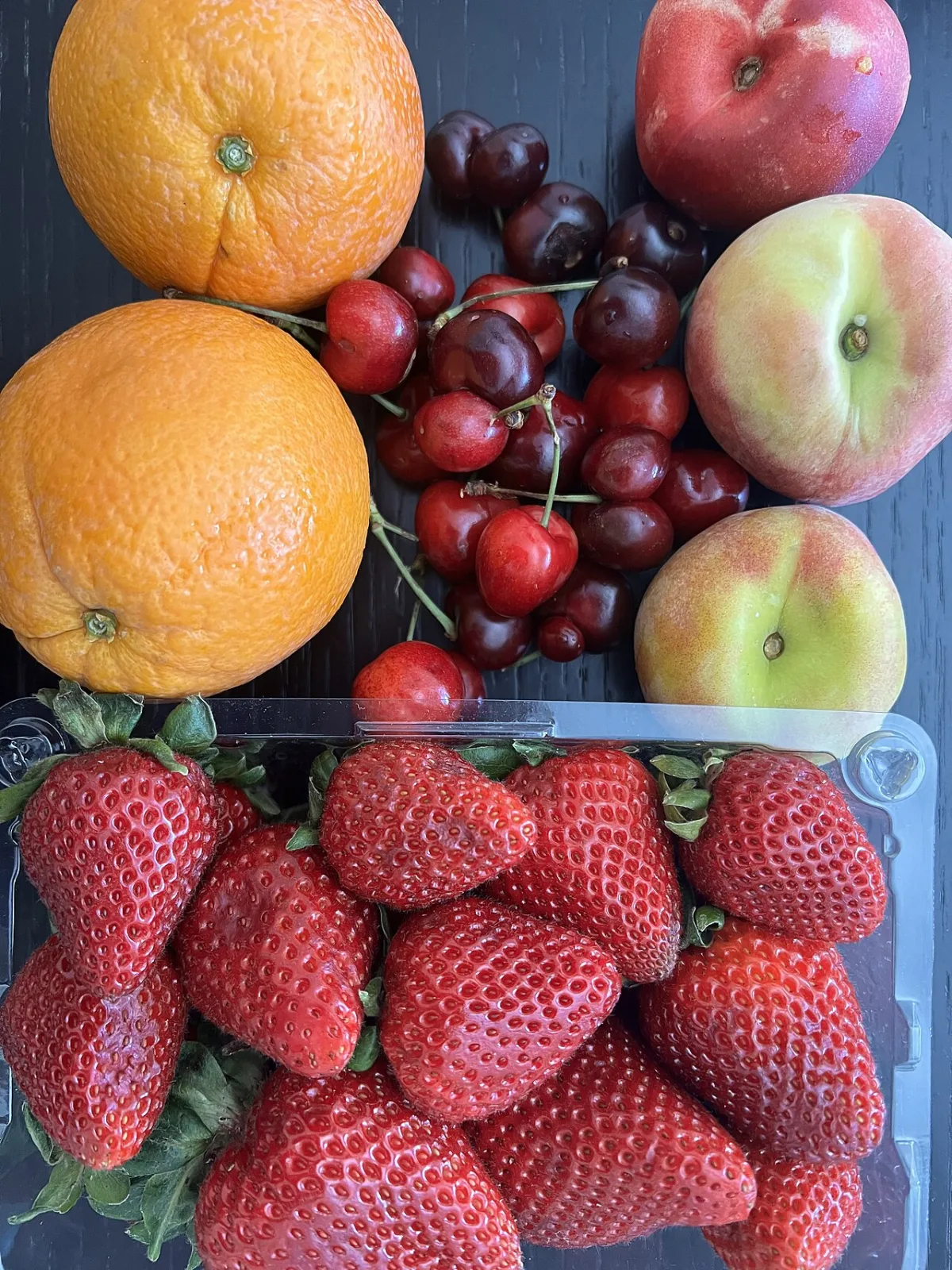Rijpe zomervruchten: perziken, kersen, sinaasappels en aardbeien naast elkaar.