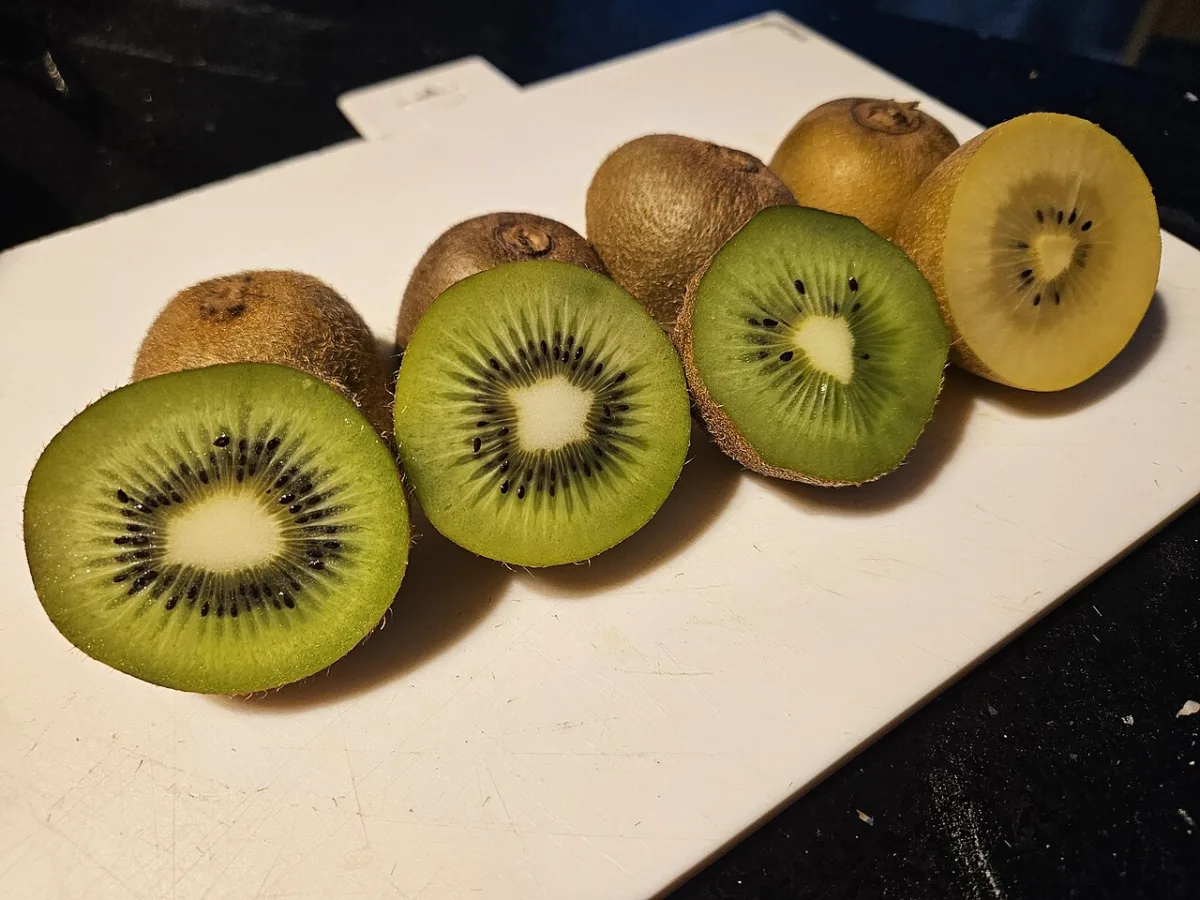 Doorgesneden groene en gele kiwi's naast elkaar op een snijplank, met hun schil ernaast.