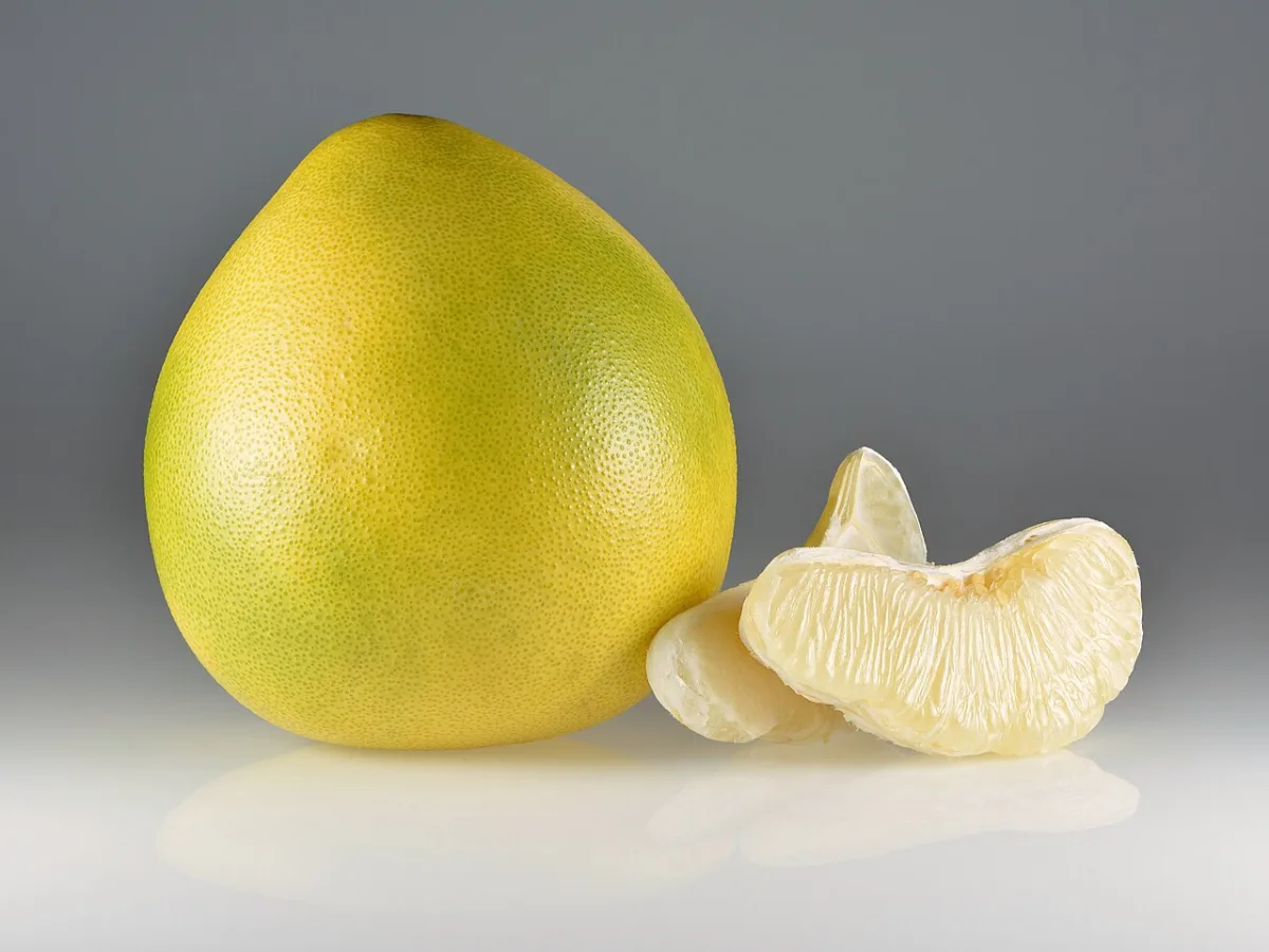 Een hele gele pomelo naast twee losse, gepelde partjes vruchtvlees.