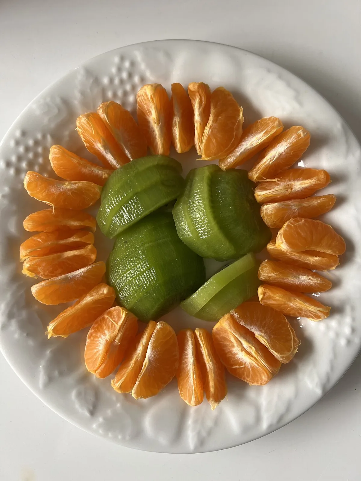 Partjes mandarijn rond plakjes kiwi op een wit bord, twee fruitsoorten rijk aan vitamine C.